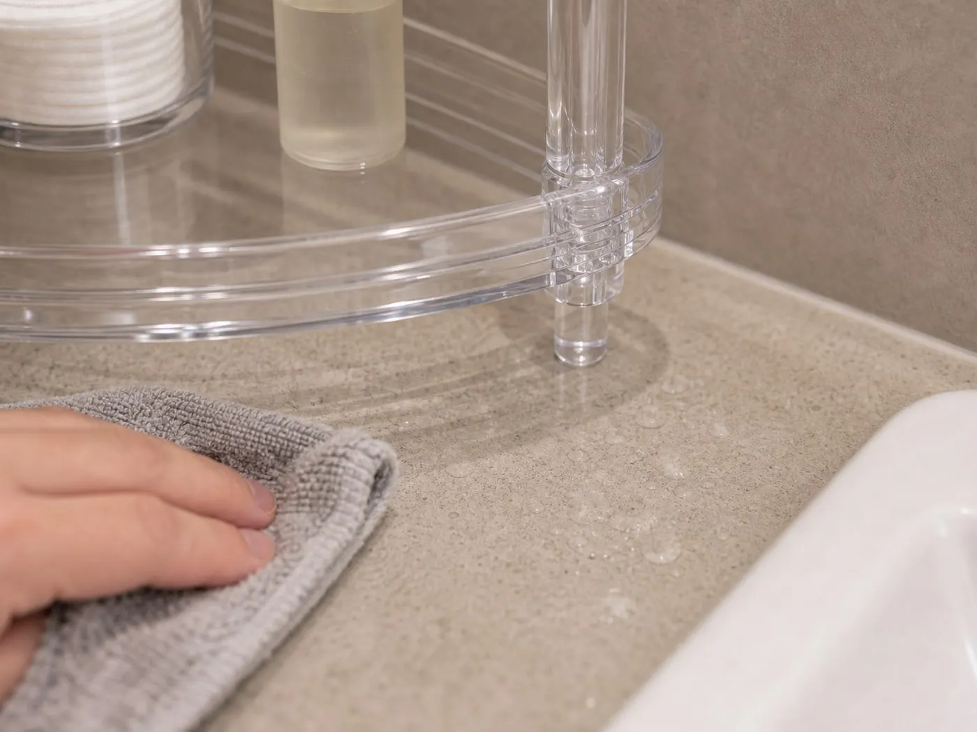 A close-up of a clear acrylic shelf edge, corner joint, foot, and vertical post connection being wiped on a bathroom counter