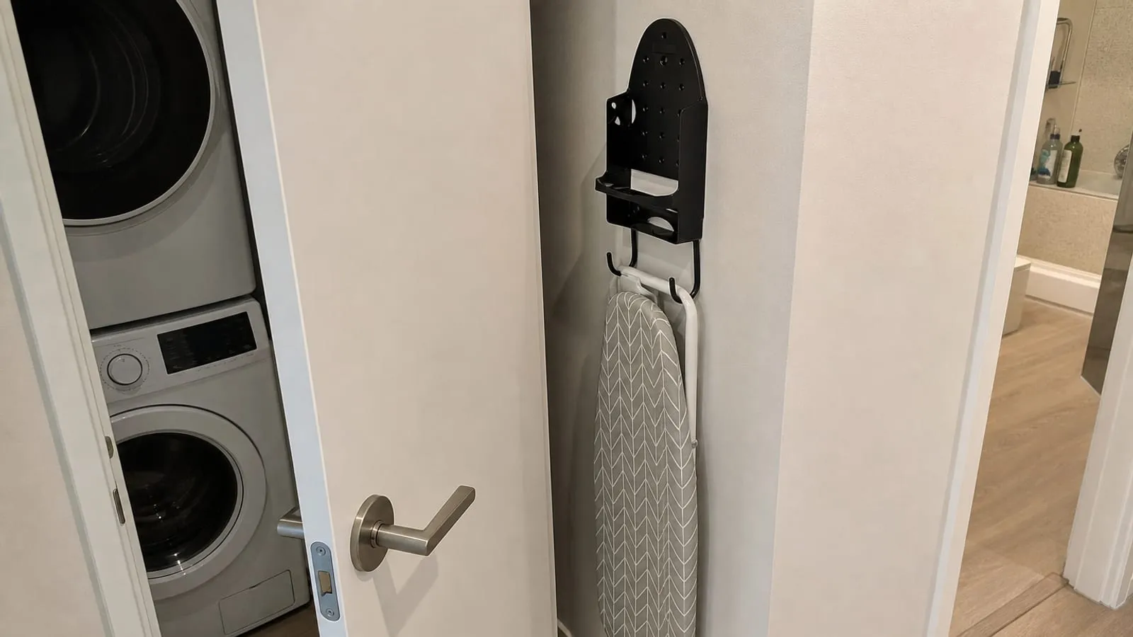 A narrow laundry closet door opened beside a wall-mounted ironing board holder to check clearance