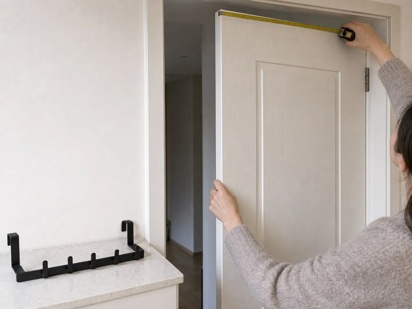 A tape measure checking the top edge of a white interior door with a black over-door hook rack nearby