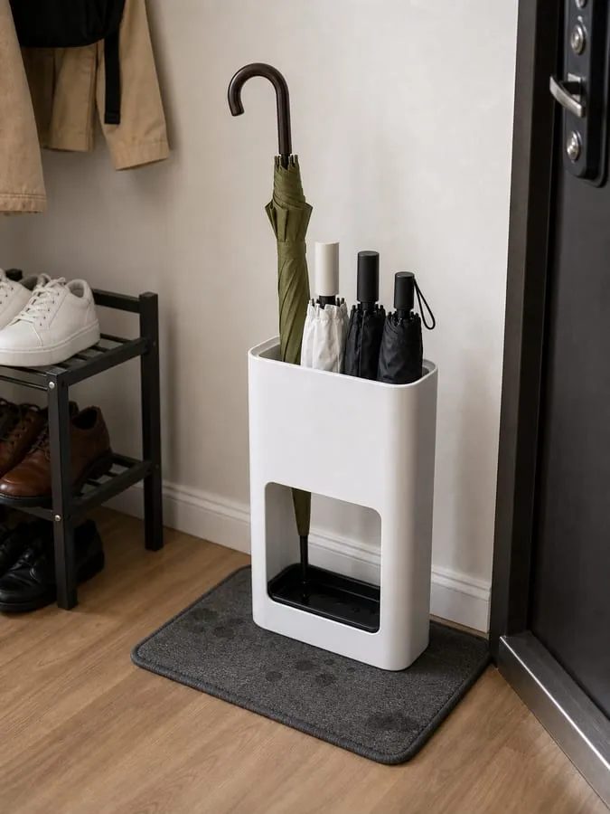 A white umbrella stand sitting on a small entry mat over a wood floor, with umbrella tips inside the tray and only slight damp marks on the mat