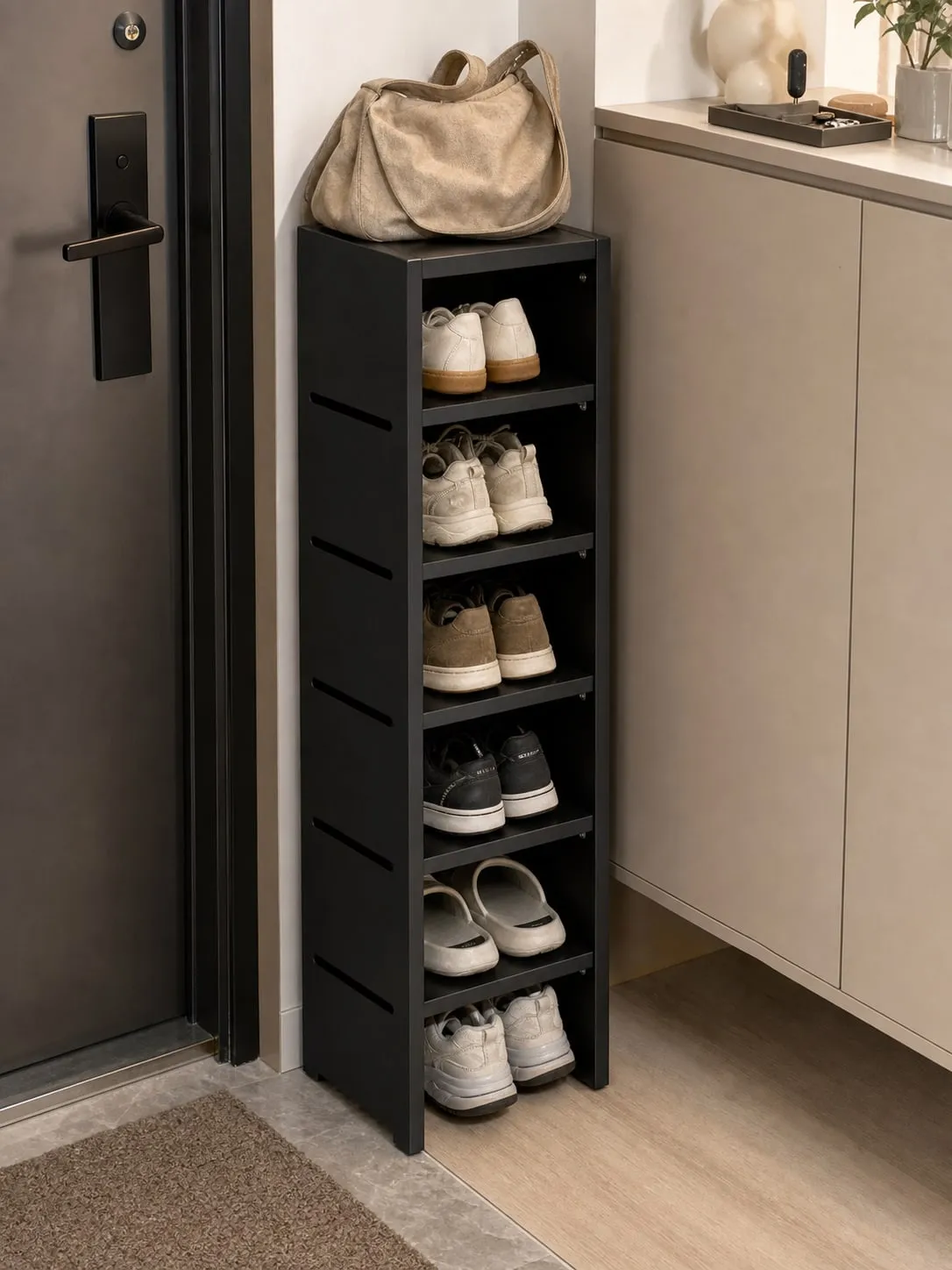A slim black shoe rack tucked beside an entryway cabinet with everyday sneakers and slippers on the lower shelves