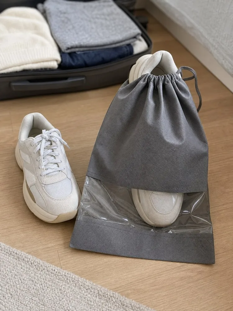 One bulky sneaker partly inside a grey shoe bag while the second shoe waits beside it