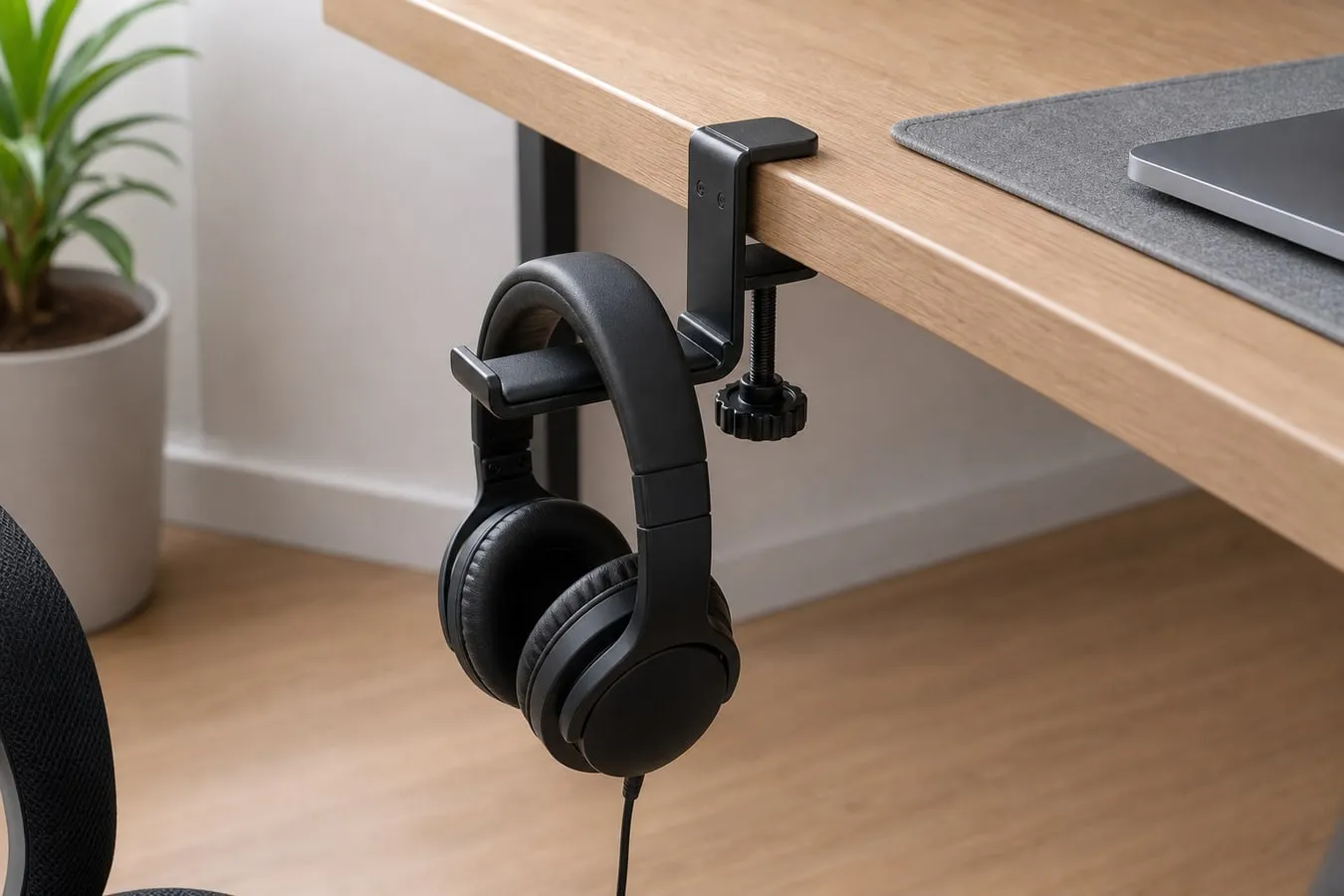 A black clamp-style headphone hanger holding only one over-ear headset by the headband with the cable hanging loosely below