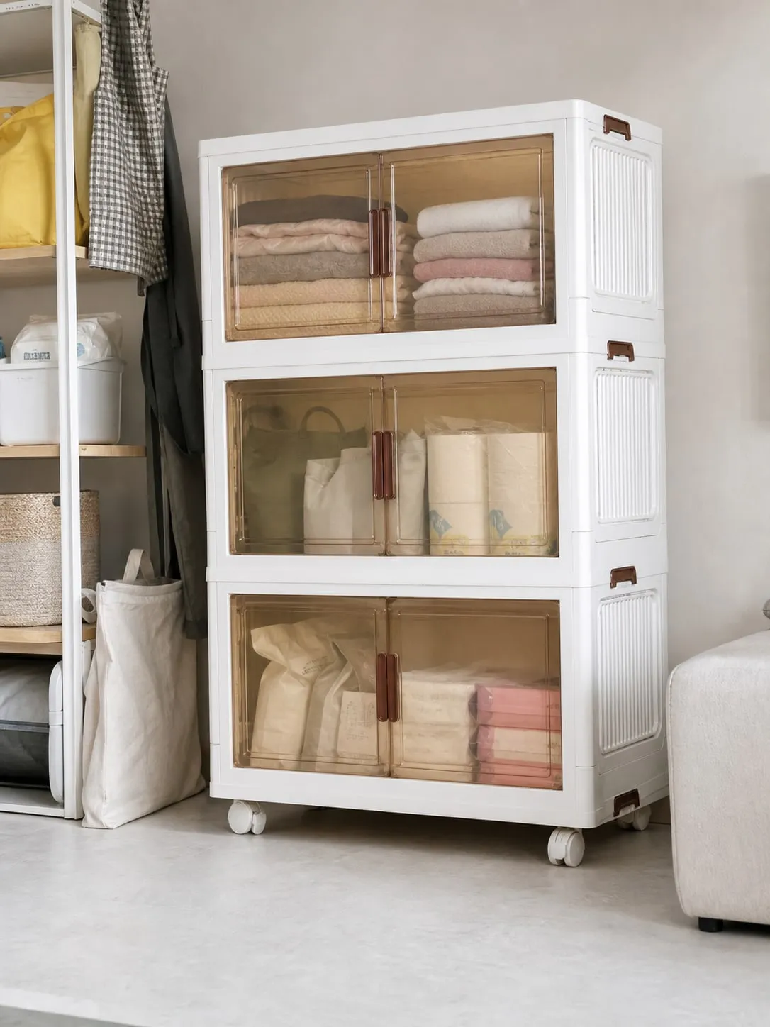White front-opening stackable storage bins beside a closet with translucent amber doors showing folded towels and paper goods inside