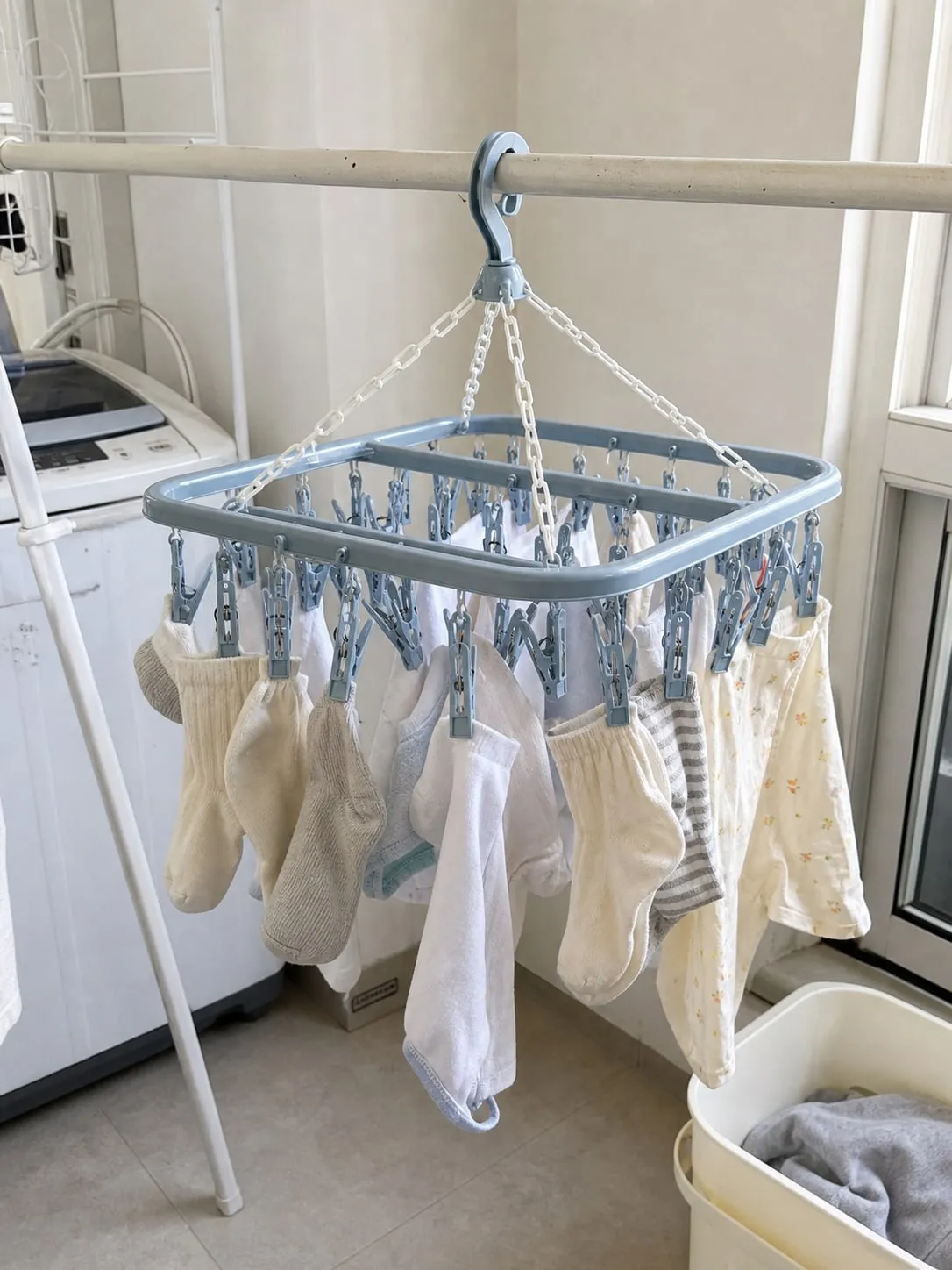 A pale blue square multi-clip drying hanger on a laundry rack holding socks and small garments with spacing between them