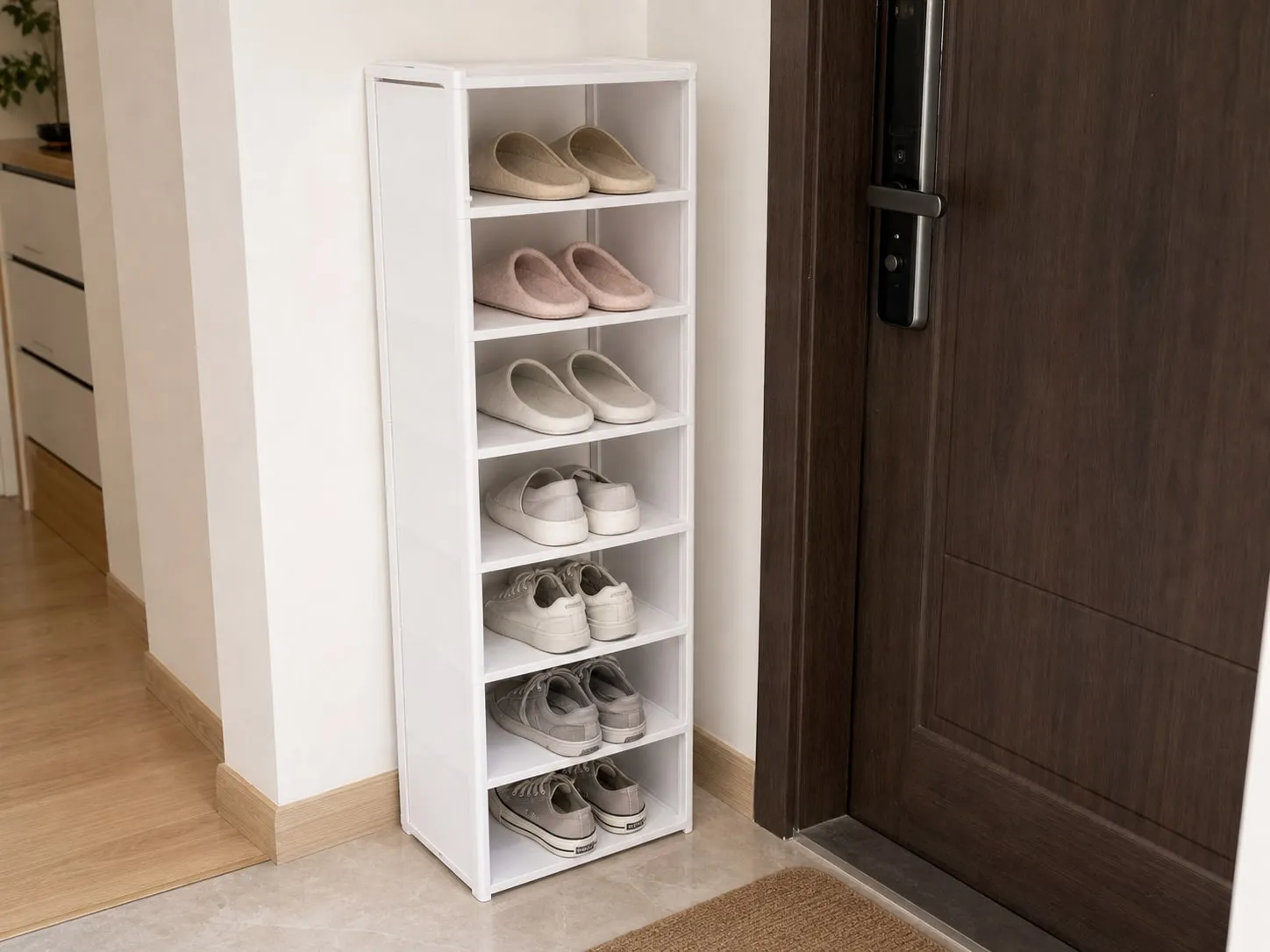 Narrow white shoe rack against a small apartment entryway wall, lightly filled with slippers and low sneakers