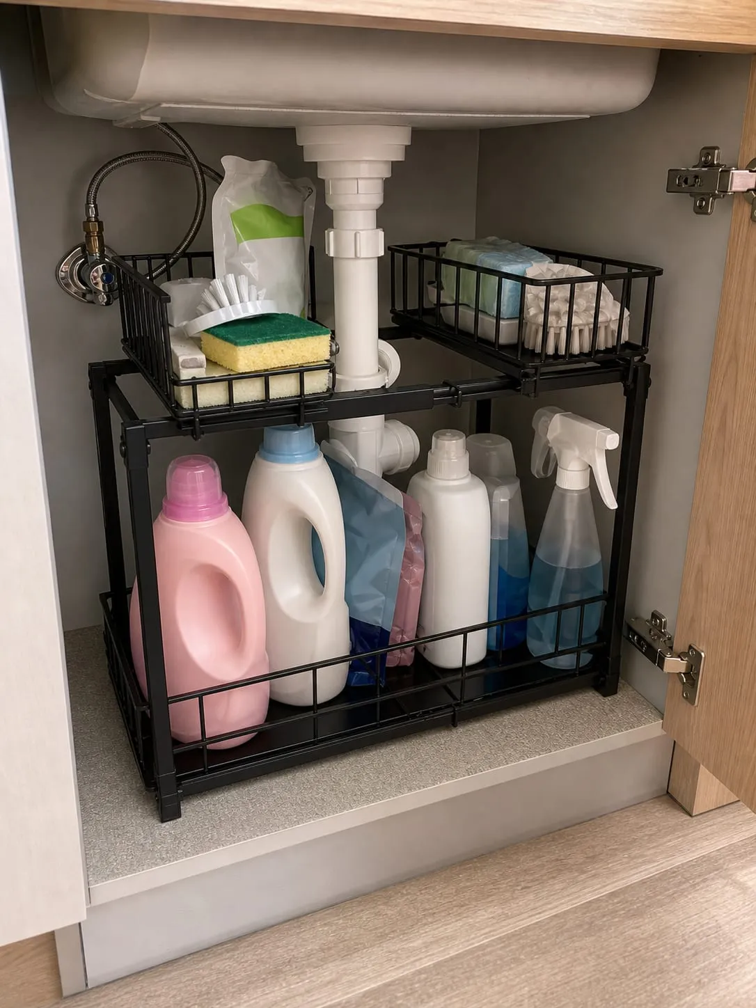 A black expandable two-tier shelf installed inside an under-sink cabinet