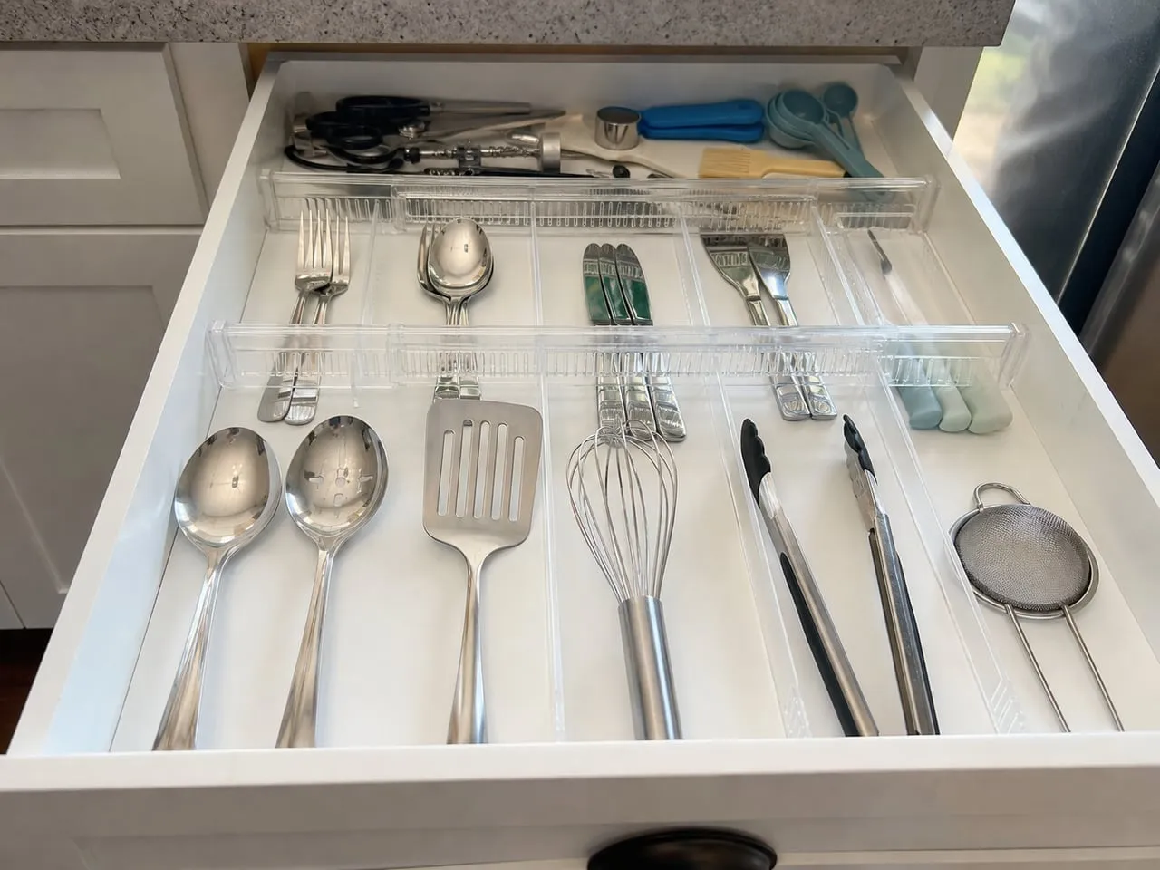 Clear adjustable dividers separating cutlery inside a white kitchen drawer