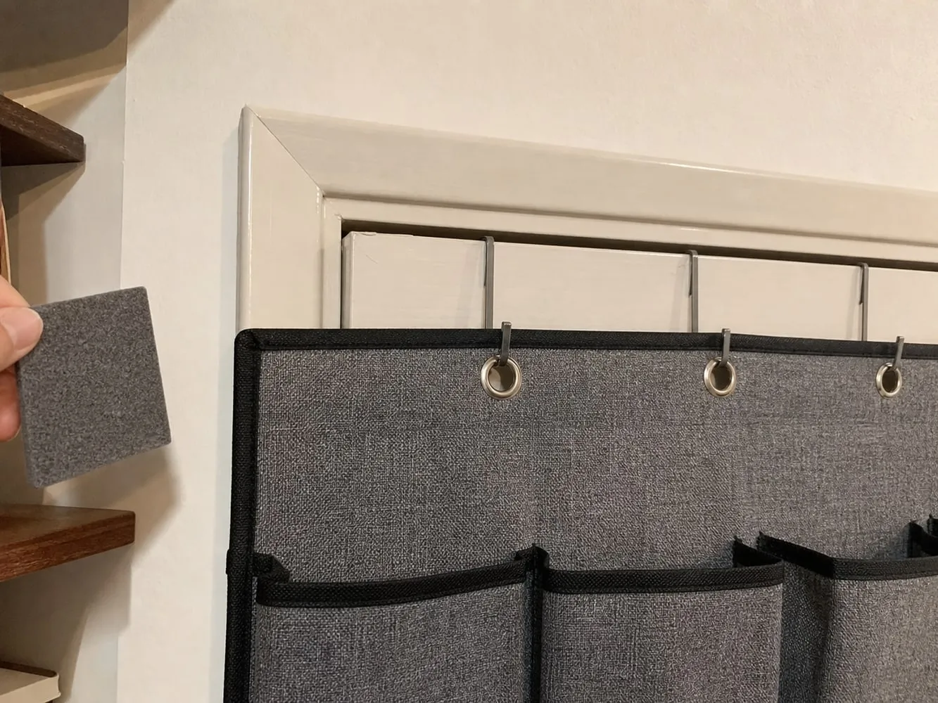 A close view of over-door hooks holding a grey pocket organizer at the top of an interior door
