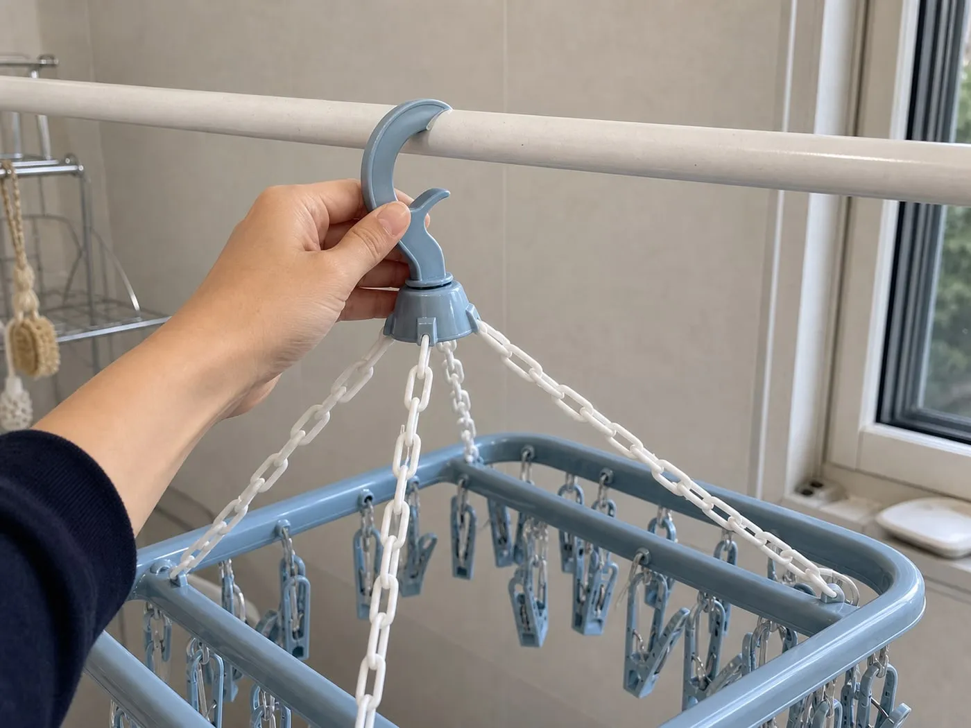 A hand checking the top hook of a pale blue multi-clip drying hanger on a white laundry rack bar
