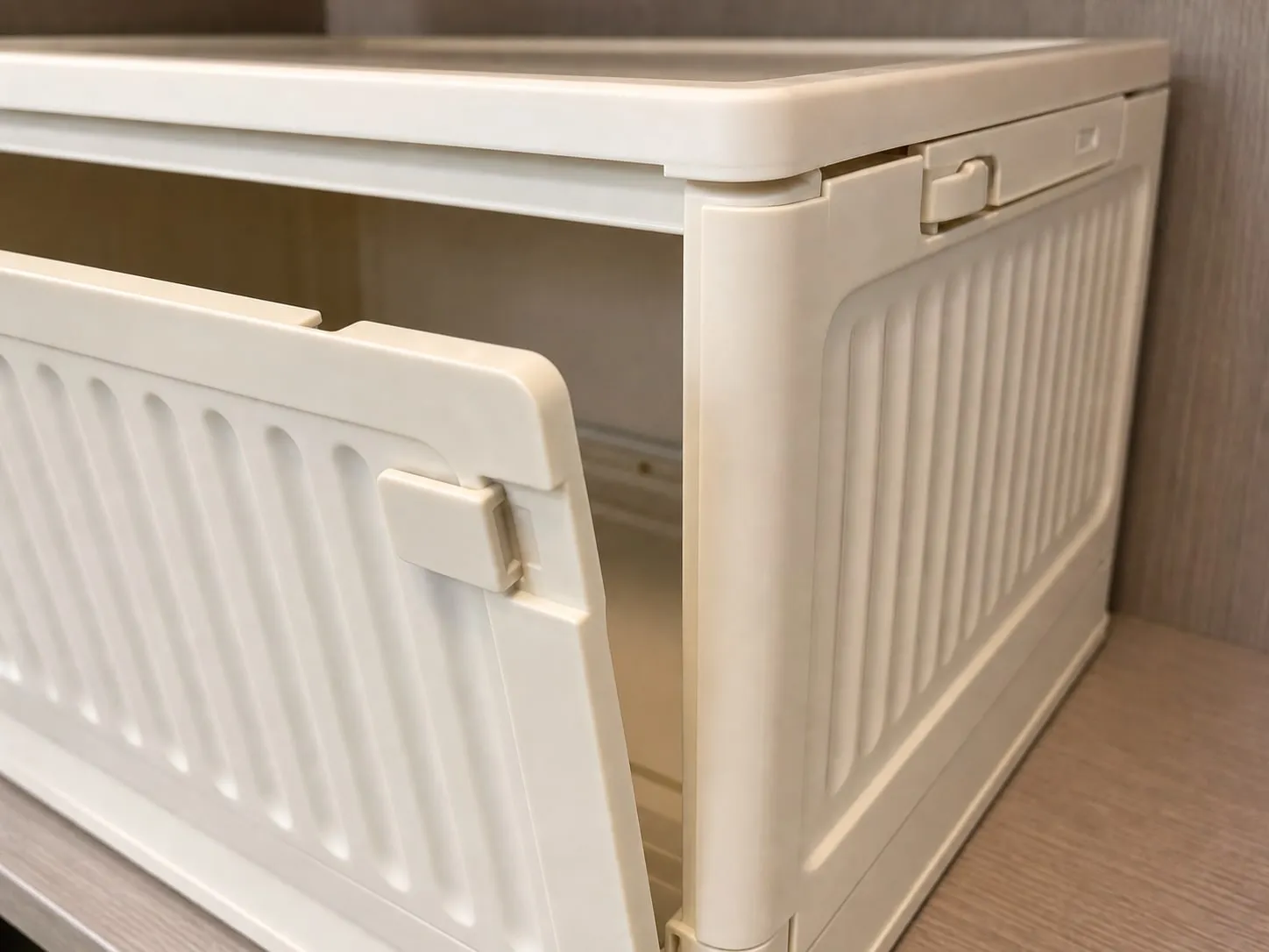 Close-up of the ribbed front panel, small latch, molded corner, and folding edge of a cream storage box
