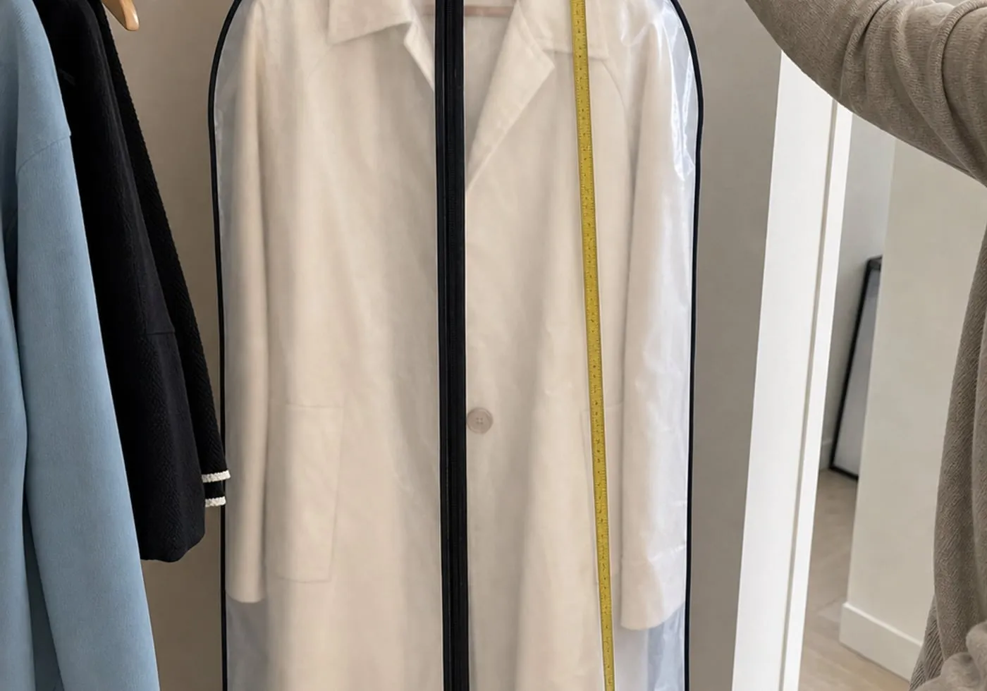 A transparent garment cover with a light coat inside, being checked with a tape measure along the garment length