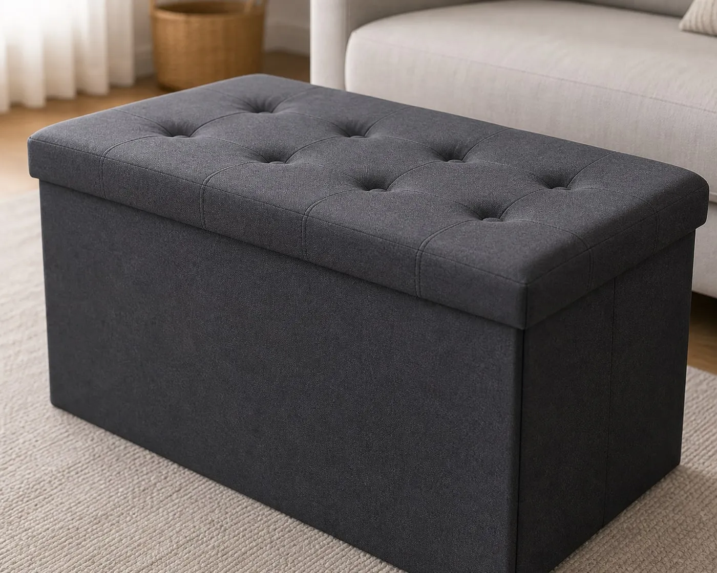 Close-up of a dark gray storage ottoman showing the padded button-tufted lid, side seam, and corner alignment
