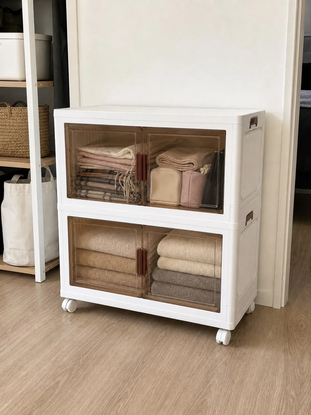 A low stack of white front-opening storage bins with folded towels in the lower layer and lighter scarves and pouches above