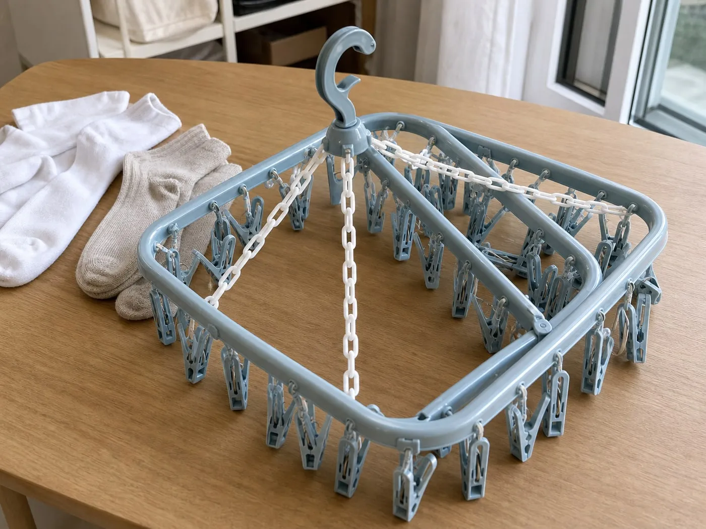 A foldable square multi-clip laundry hanger partly folded on a table beside several socks