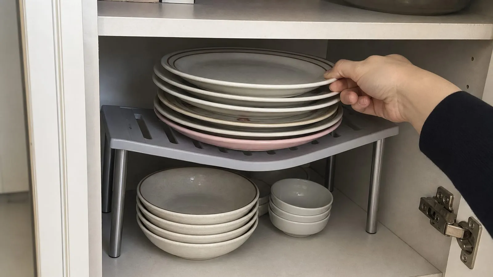 Too many plates on a raised shelf riser while one hand carefully removes a plate