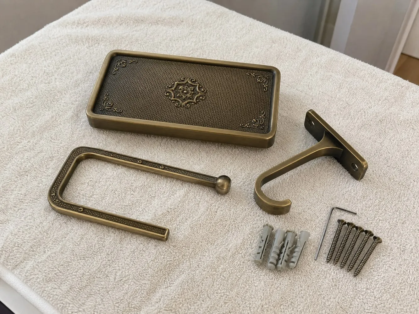 Uninstalled shelf-style toilet paper holder parts, screws, and anchors laid out on a towel