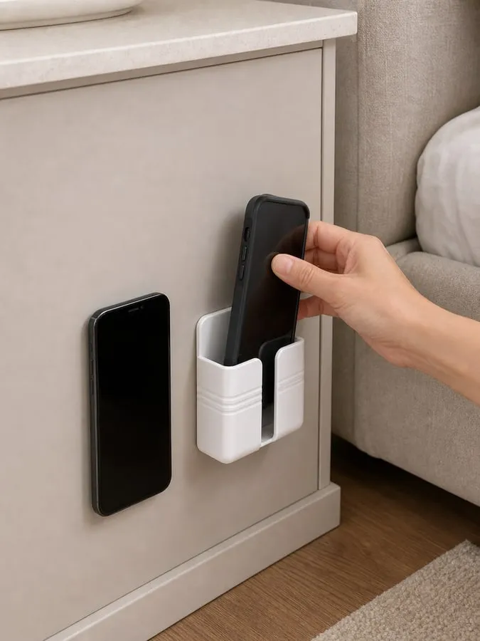 A phone in a thicker case being checked against the depth and front lip of a small white wall-mounted holder near a bedside panel