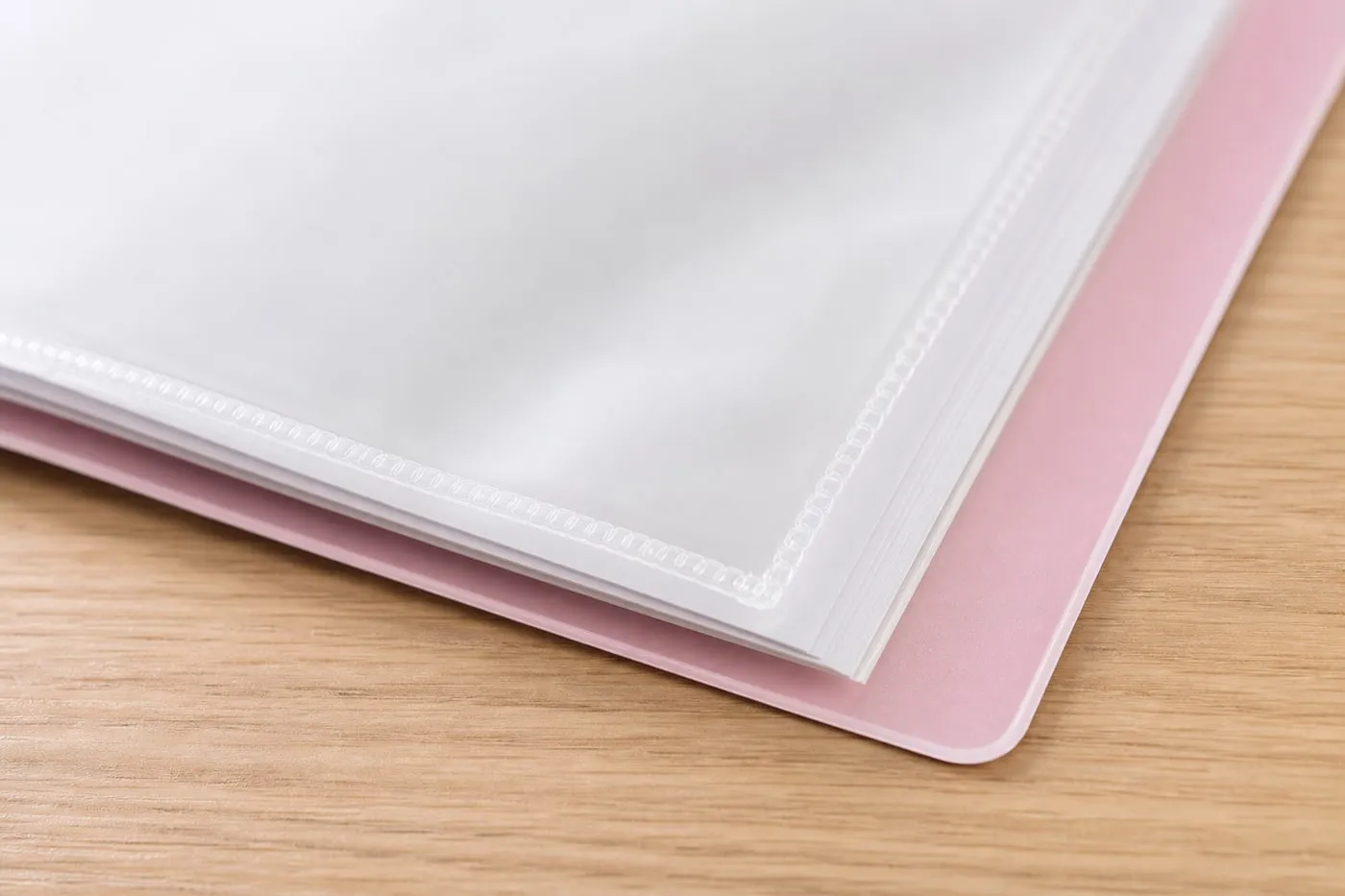 Close-up of a pastel pink A4 pocket folder showing the transparent sleeve seam and rounded cover corner