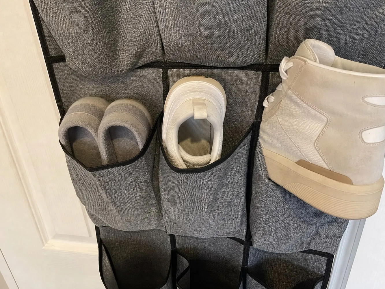 Low slippers and a small sneaker in grey organizer pockets, with a bulky high-top sneaker placed outside the pocket