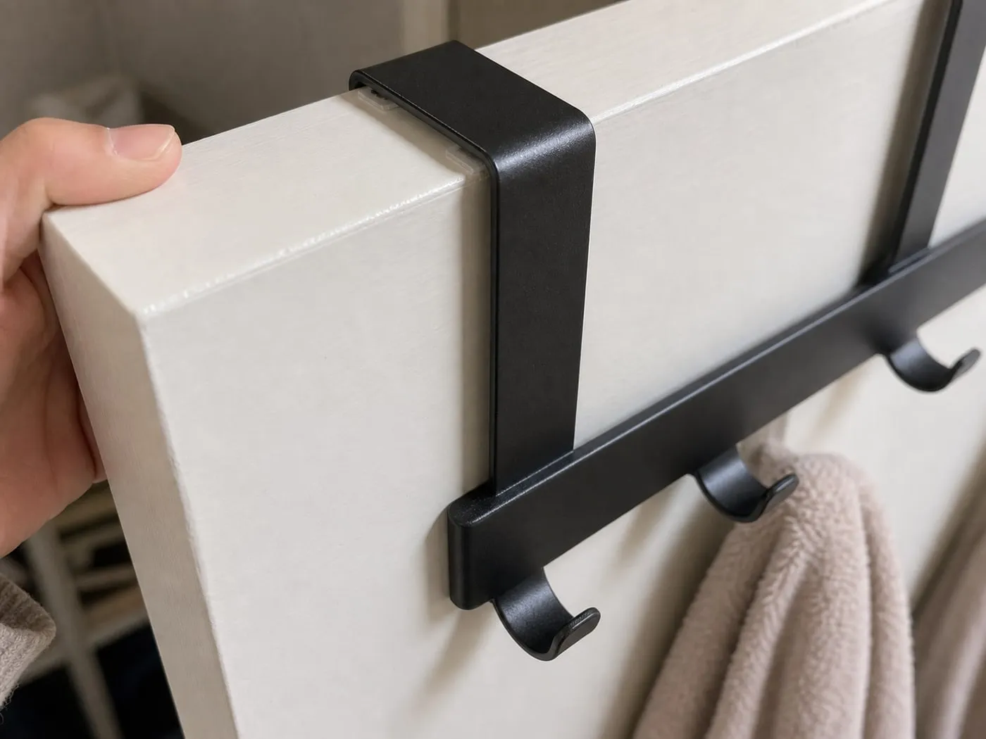 A close-up of a black over-door hook rack bracket sitting over the top of a white door