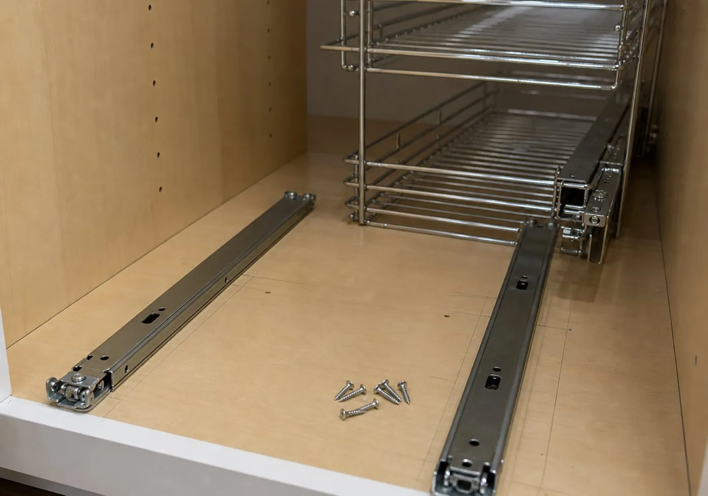 Two metal rails aligned in parallel on a wooden cabinet bottom with screws and pencil marks nearby