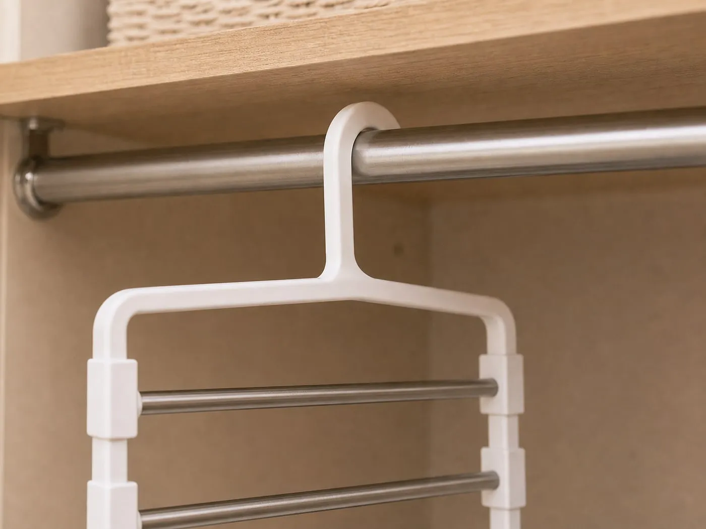 Close-up of the white top hook of the pants hanger resting on a round metal closet rod