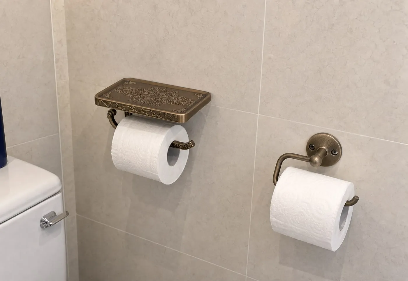 A shelf-style toilet paper holder and a simpler wall-mounted roll holder installed on nearby tile walls