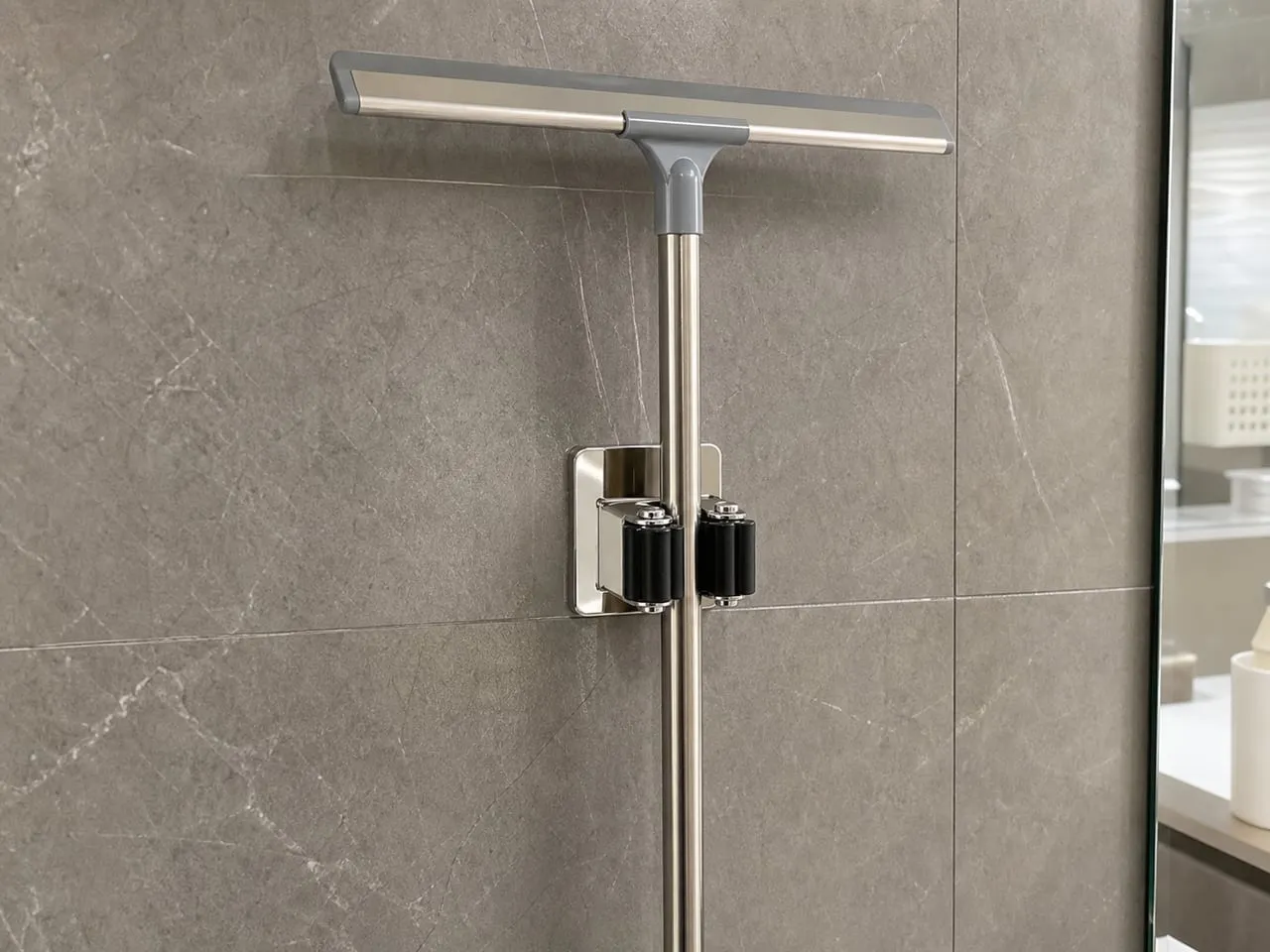 A stainless single wall clip holding one squeegee on a tile wall