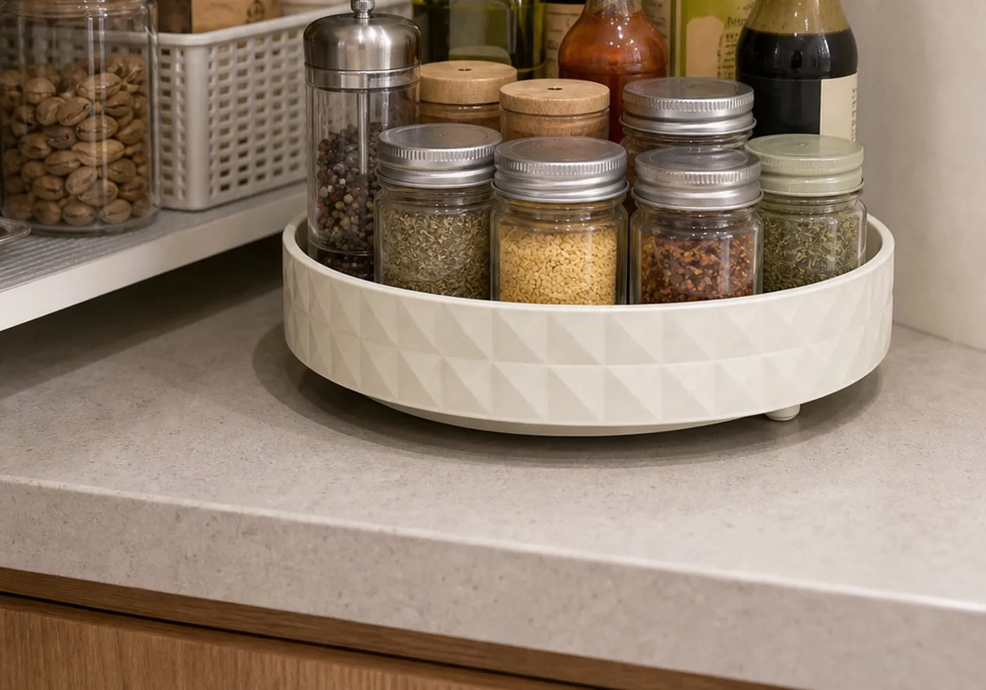A white single-tier round rotating tray on a kitchen shelf with closed spice jars and sealed bottles