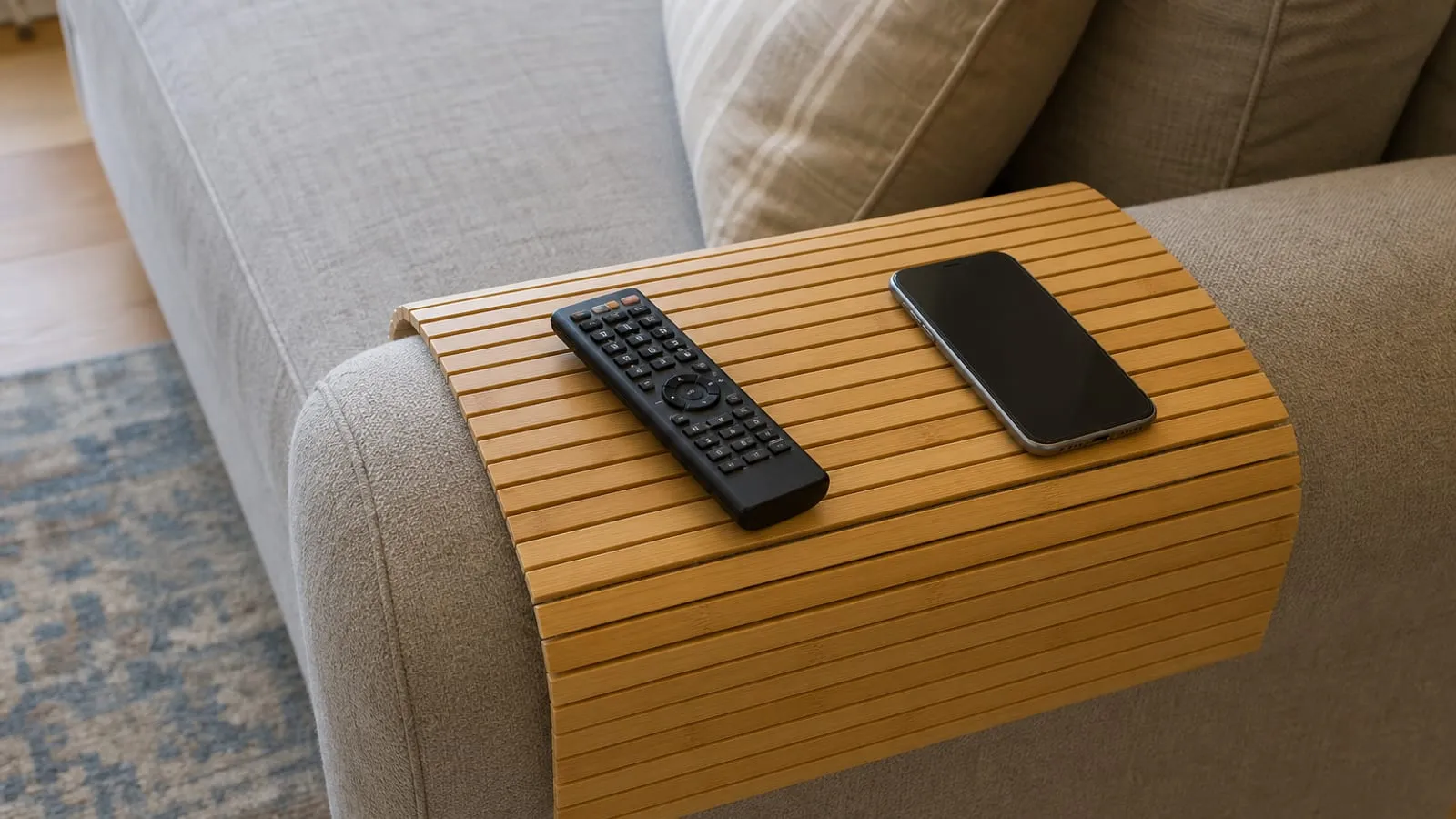 Slatted bamboo sofa-arm tray draped over a broad fabric arm with a remote and phone on top