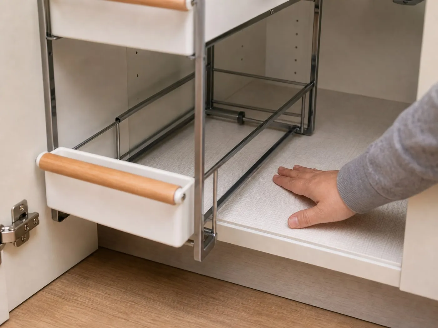 A close-up of the white pull-out organizer base and rail area being checked by hand on a lower cabinet floor
