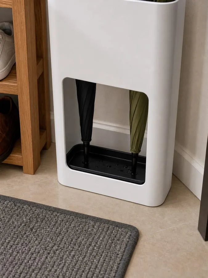 Close-up of the lower front opening of a white umbrella stand with umbrella tips resting in the black tray and a few small droplets inside