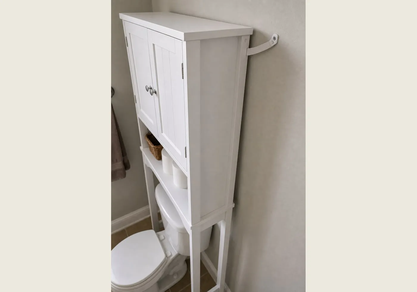 A rear-side view of a white over-toilet cabinet near the wall with a small generic wall strap area visible