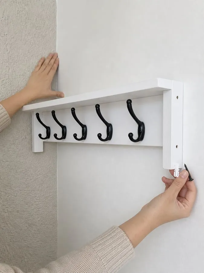 A hand holding a wall anchor and screw beside a white rack while smooth and textured wall surfaces are visible