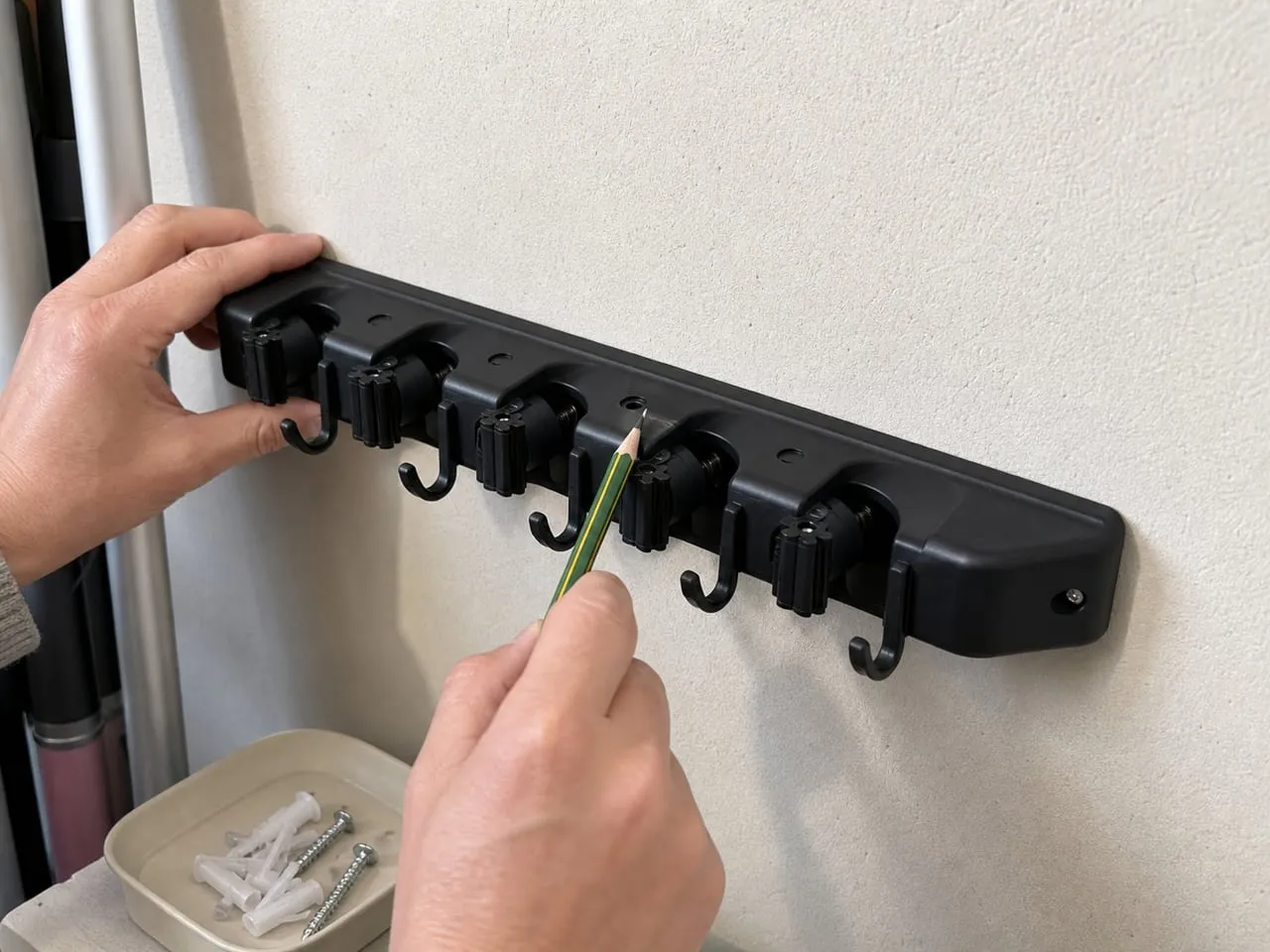 Checking screw positions for a black wall-mounted cleaning-tool holder