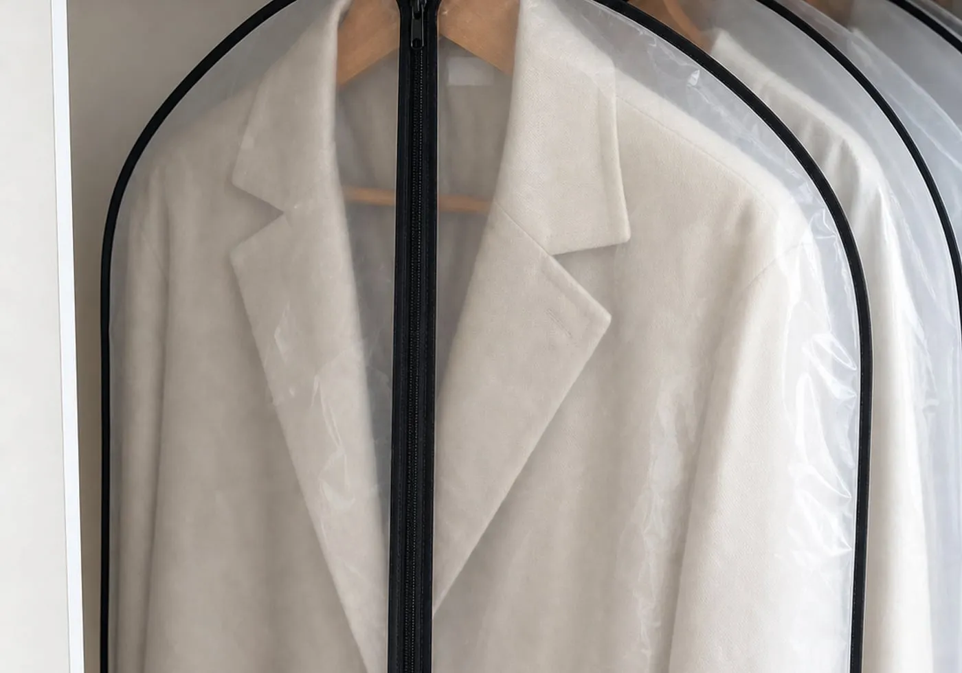 A close-up of a transparent garment cover showing the black zipper line, hanger opening, and a jacket inside